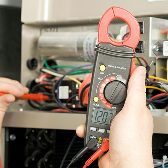 Technician using a multimeter to check a furnace's electrical connections.