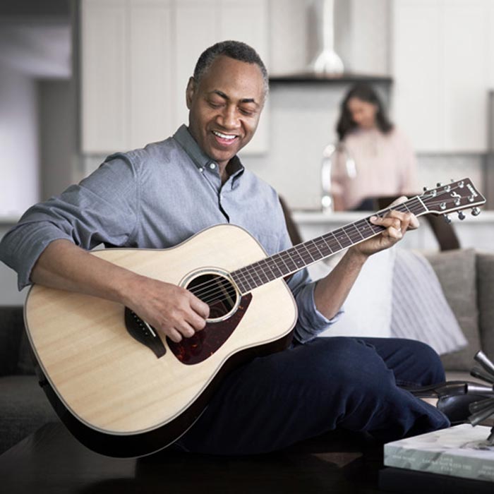 Man playing an acoustic guitar while sitting on a couch at home.