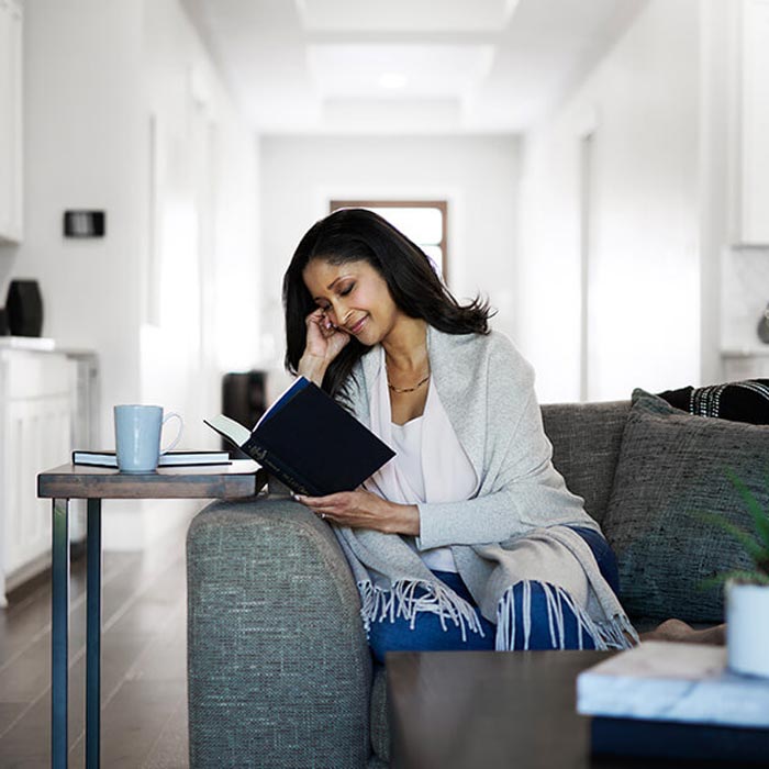 Woman sitting on a couch reading a book in a cozy living room.