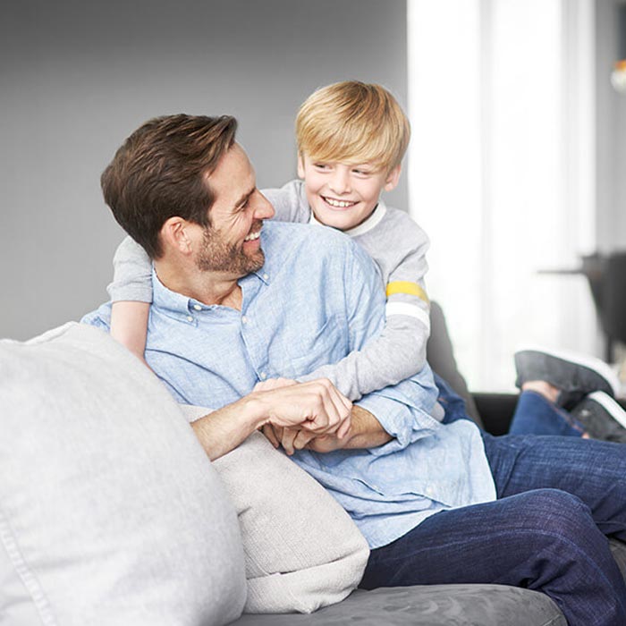 Father and son smiling and playing on a couch in a cozy living room.