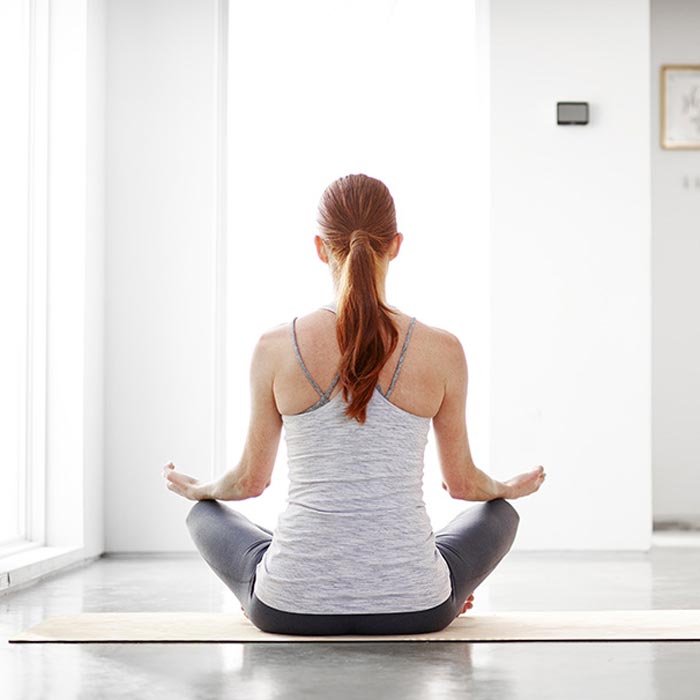 Woman sitting cross-legged on a yoga mat, meditating in a bright room.